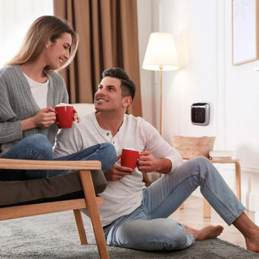 Paar mit Tassen entspannt im warmen Wohnzimmer, WellHeater an der Wand